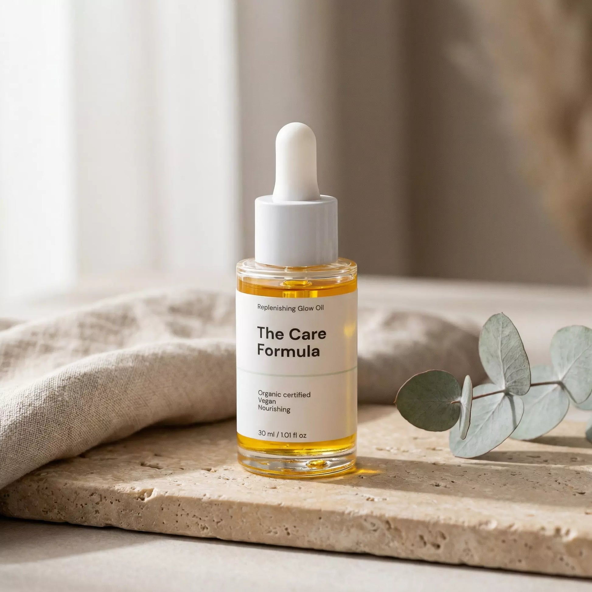 The Care Formula Replenishing Glow Oil golden facial oil lifestyle scene on a neutral background with eucalyptus leaves.