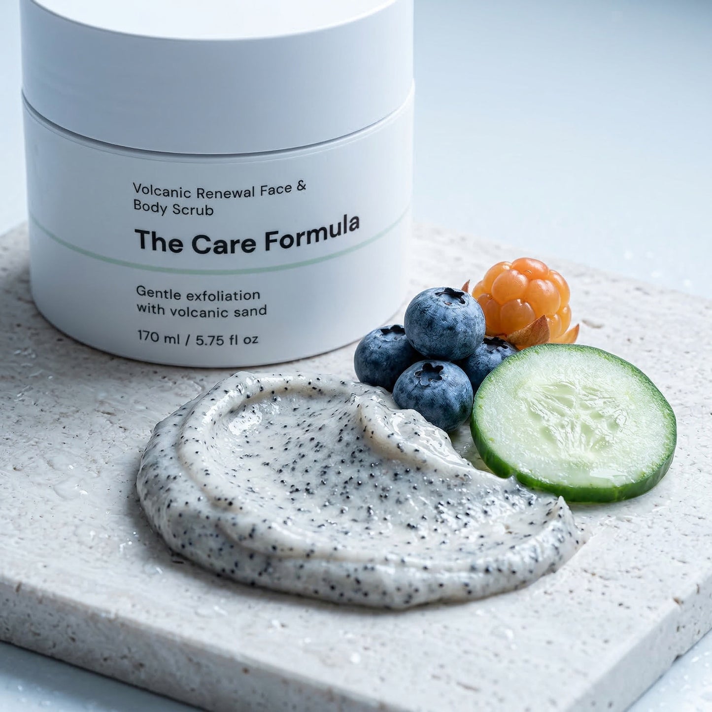 The Care Formula Volcanic Renewal Face & Body Scrub key ingredients with a scoop of scrub and fresh fruits on a light surface.
