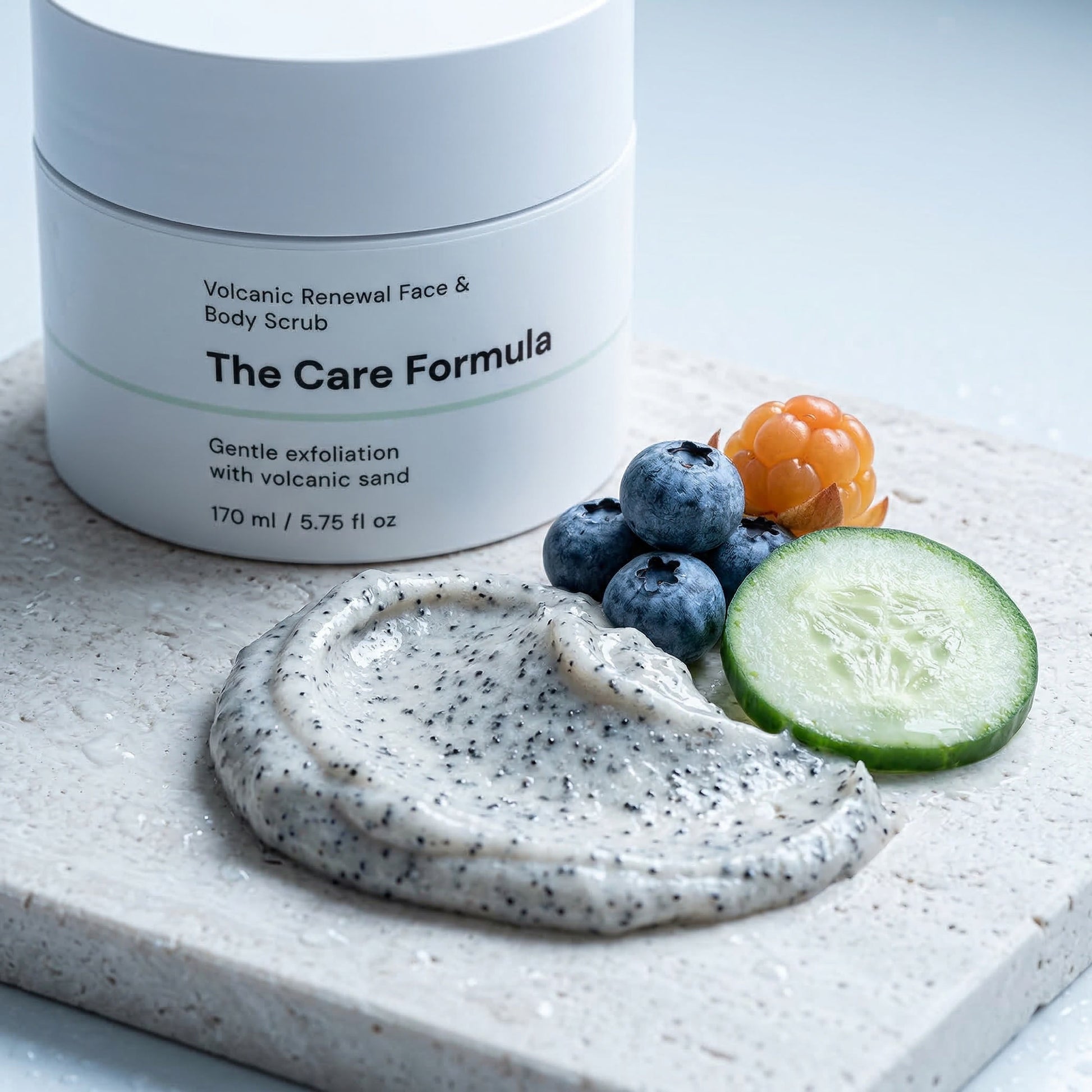 The Care Formula Volcanic Renewal Face & Body Scrub key ingredients with a scoop of scrub and fresh fruits on a light surface.