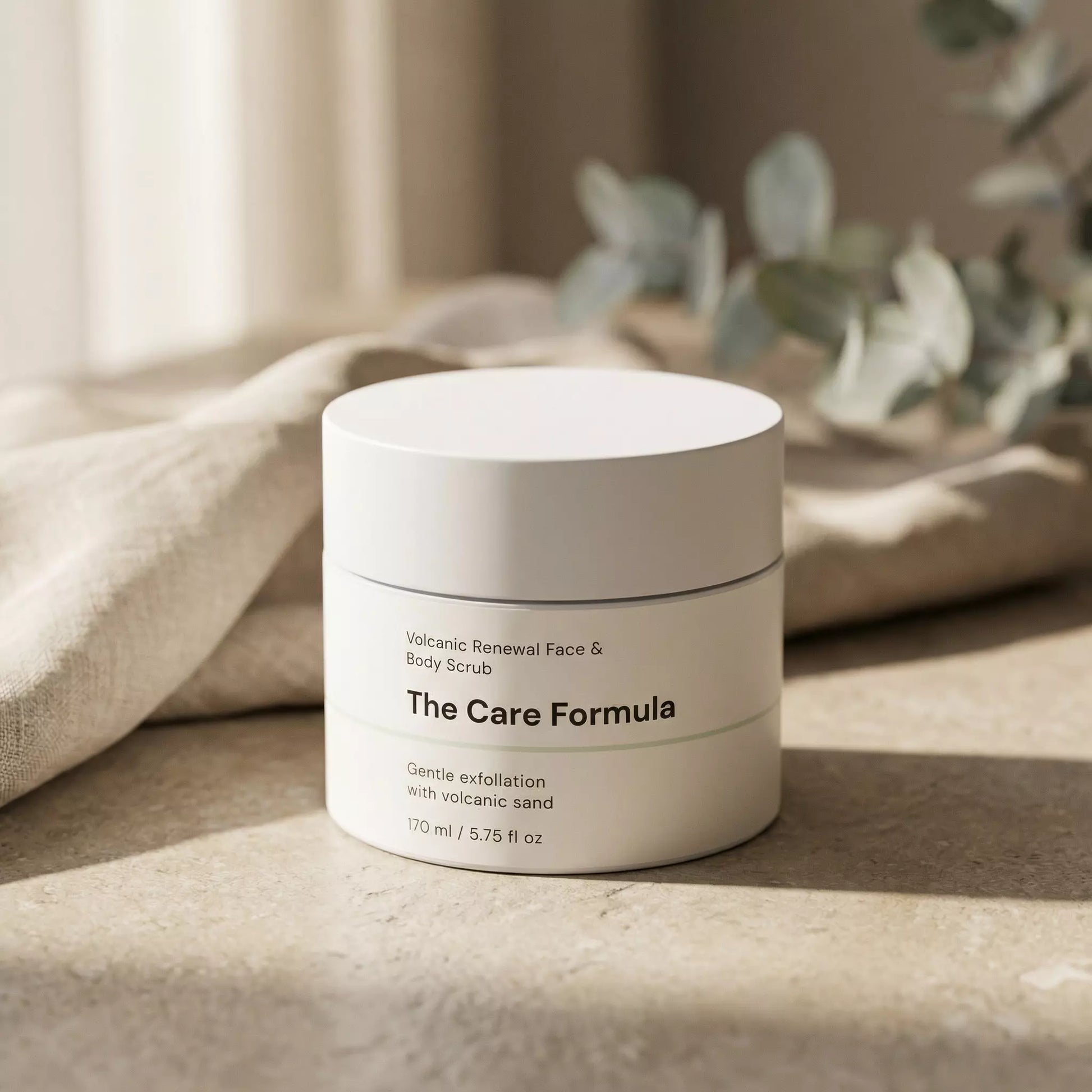 The Care Formula Volcanic Renewal Face and Body Scrub skincare exfoliating lifestyle scene on neutral stone surface